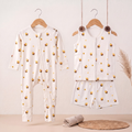 A baby two-piece outfit set hanging on wooden hangers against a light beige wall. The set includes a long-sleeve zip-front bamboo sleepsuit and a matching sleeveless bamboo jabla and shorts set, both in white with a repeating yellow honeybee print.