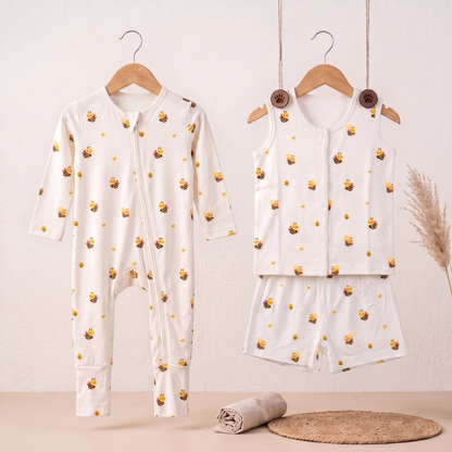 A baby two-piece outfit set hanging on wooden hangers against a light beige wall. The set includes a long-sleeve zip-front bamboo sleepsuit and a matching sleeveless bamboo jabla and shorts set, both in white with a repeating yellow honeybee print.