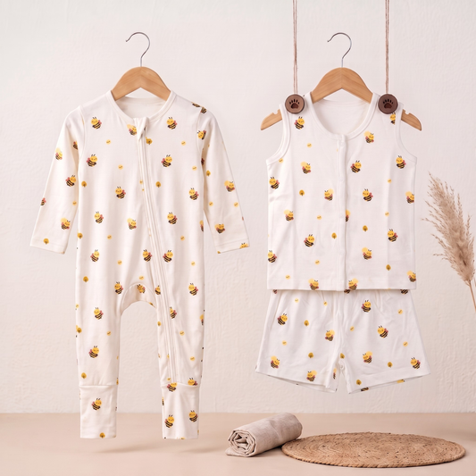 A baby two-piece outfit set hanging on wooden hangers against a light beige wall. The set includes a long-sleeve zip-front bamboo sleepsuit and a matching sleeveless bamboo jabla and shorts set, both in white with a repeating yellow honeybee print.