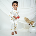 A smiling young boy wearing a white long-sleevebamboo lounge set with small yellow and black bee prints, holding a small red toy against a soft white draped backdrop.