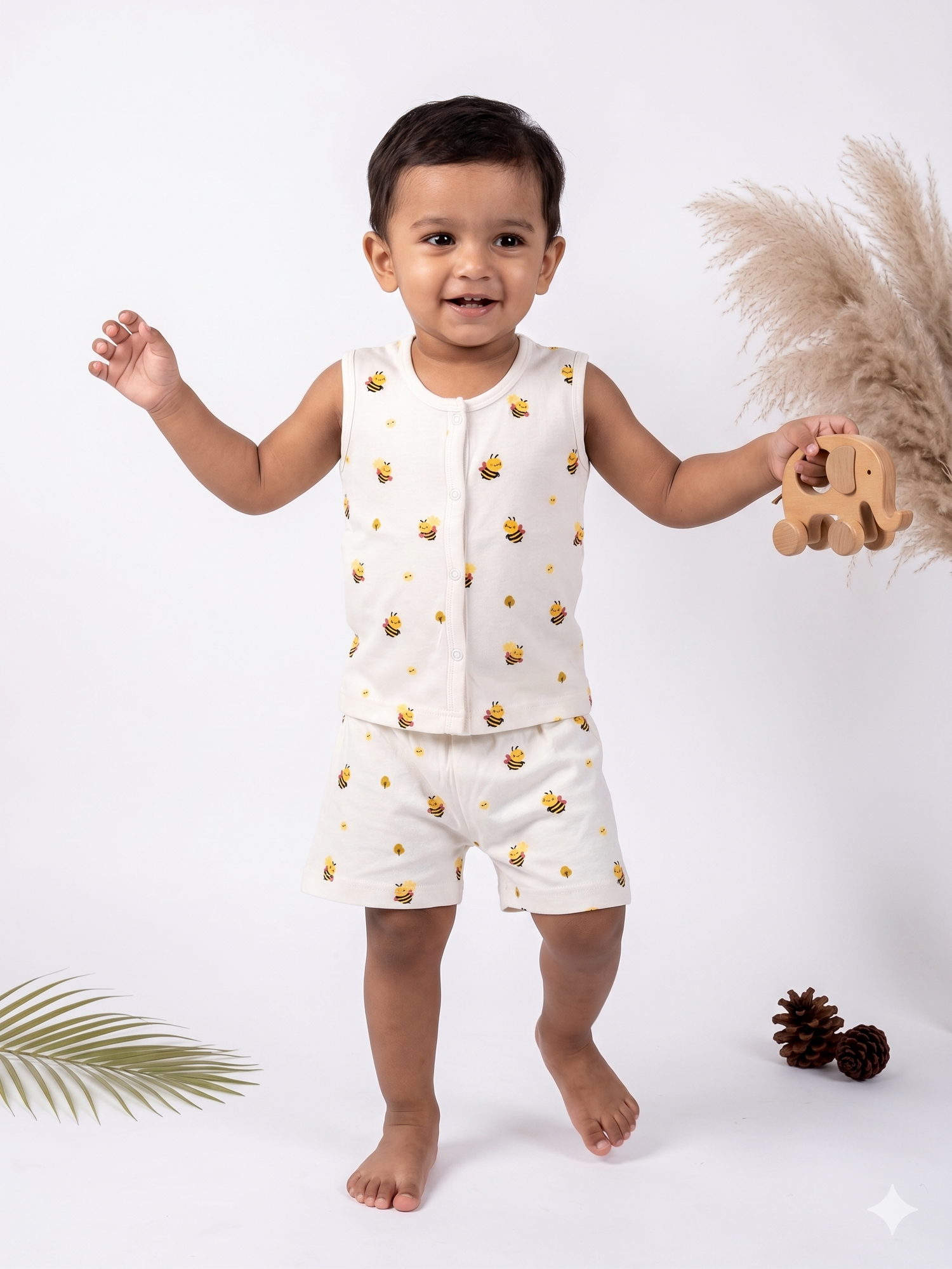 Child wearing a white outfit with yellow patterns, holding a toy, on a white background