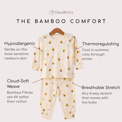 A baby bamboo lounge set consisting of a long-sleeve top and matching pants, displayed on a wooden hanger against a light beige background. The pajamas are cream-colored with a repeating pattern of small yellow and black bumblebees.