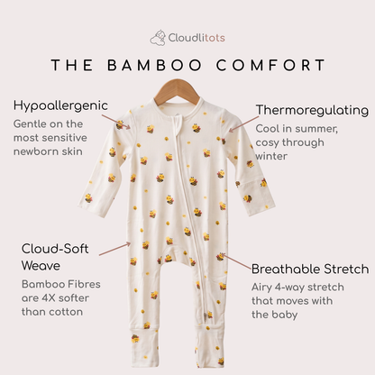 An off-white long-sleeve baby bambii sleepsuit with a yellow and brown bee pattern, hanging on a wooden hanger against a light beige background. The image features text callouts highlighting key features: 'Hypoallergenic', 'Thermoregulating', 'Cloud-Soft Weave', and 'Breathable Stretch'.