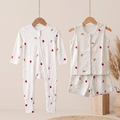 A baby bamboo sleepsuit and jabla shorts set displayed on wooden hangers against a warm beige background. The set includes a long-sleeve footless zip-front sleeper with a small red berry and light pink floral print, and a matching sleeveless vest and shorts set in the same fabric.