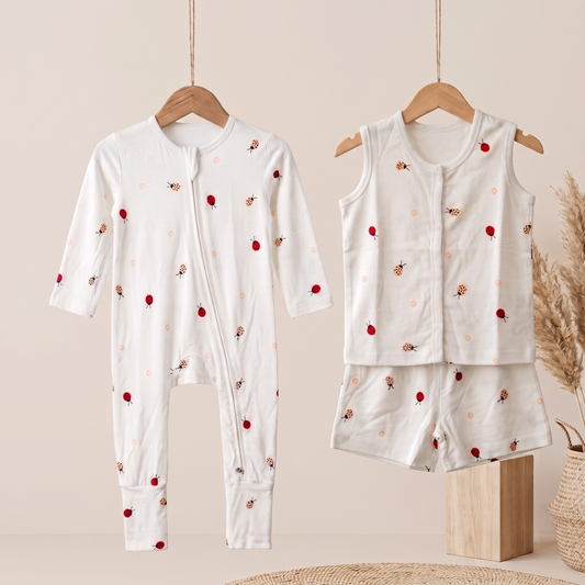 A baby bamboo sleepsuit and jabla shorts set displayed on wooden hangers against a warm beige background. The set includes a long-sleeve footless zip-front sleeper with a small red berry and light pink floral print, and a matching sleeveless vest and shorts set in the same fabric.