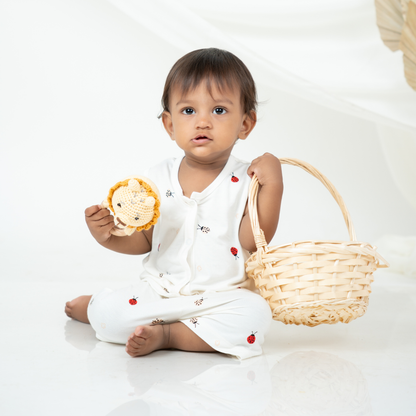 A baby sitting on a white studio floor wearing a white bamboo jabla shorts set, holding a small woven basket and a plush lion toy.