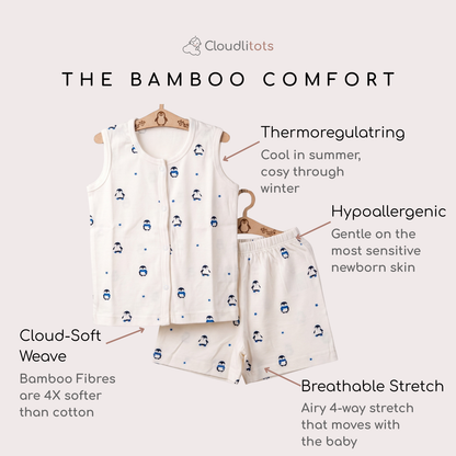 A baby two-piece clothing set consisting of a sleeveless bamboo jabla and matching shorts in a warm off-white color, printed with a small blue penguin pattern. The set is displayed on wooden hangers against a light beige background with descriptive text callouts highlighting its features: thermoregulating, hypoallergenic, Cloud-Soft Weave, and breathable stretch.