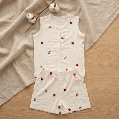 A baby bamboo jabla and shorts set consisting of a sleeveless button-front top and matching shorts in off-white, decorated with small red ladybugs and tiny yellow-and-black bees. The set is styled flat-lay on a beige linen cloth with cotton bolls on a light wood background.